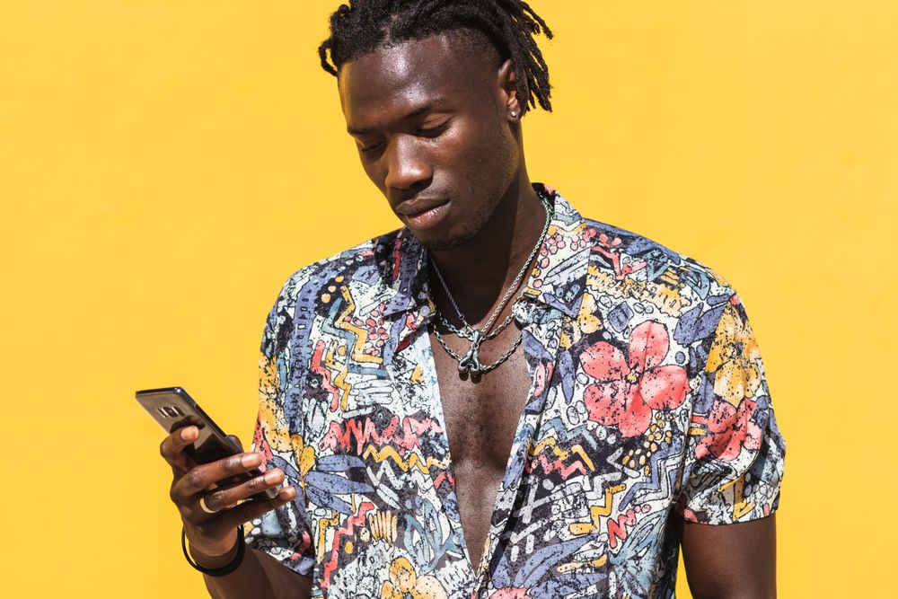 Stylish Black man in colorful shirt with smartphone