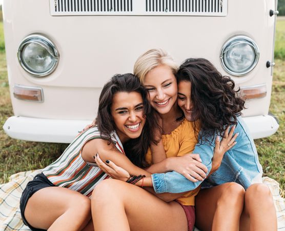 Three friends sitting together in front of a beige van