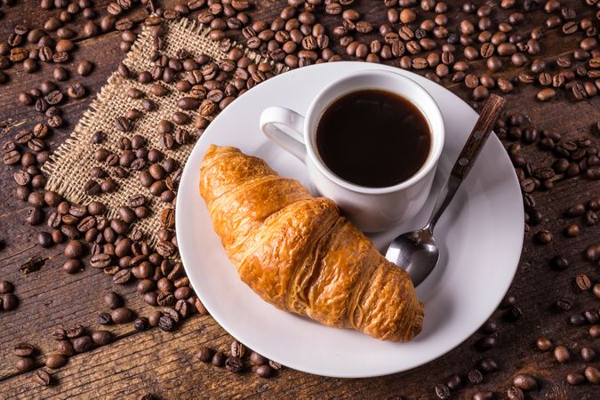 Coffee and croissant surrounded by coffee beans