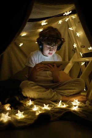 Focused boy browsing tablet on blanket fort
