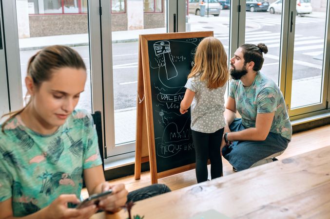Restaurant owners managing family and work balance with daughter drawing on board