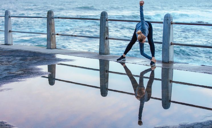 Reflection on wet road of woman doing stretches