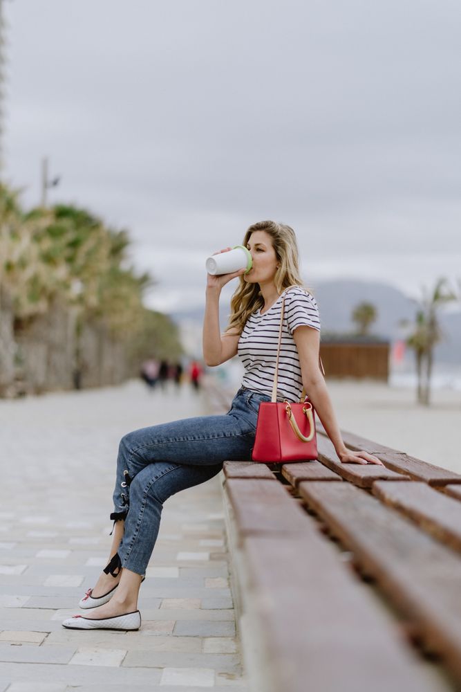 Happy woman with disposable cup of coffee sitting on street bench
