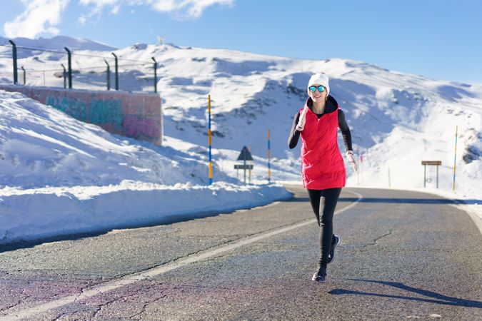 Woman in wintry gear running on road in the mountains on cold day
