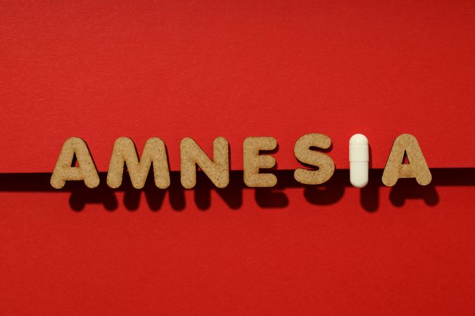 Cork letters of the word “Amnesia” with pill on red background in straight line