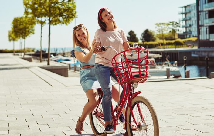 Two happy women riding a bicycle along the waterfront