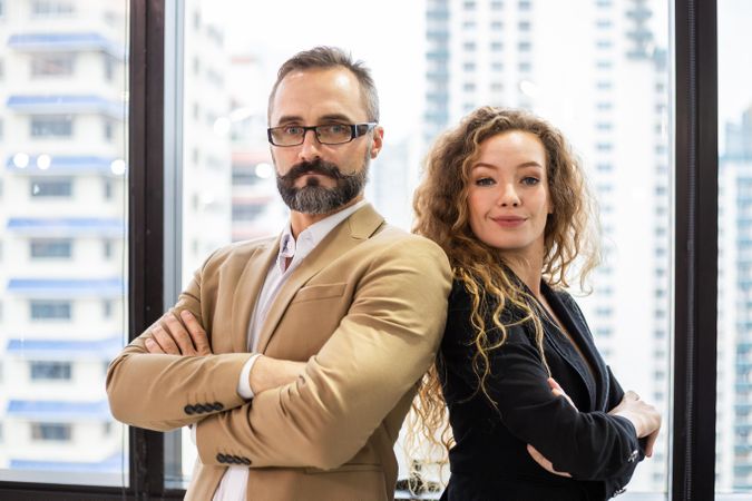 Confident man and woman standing tall in office