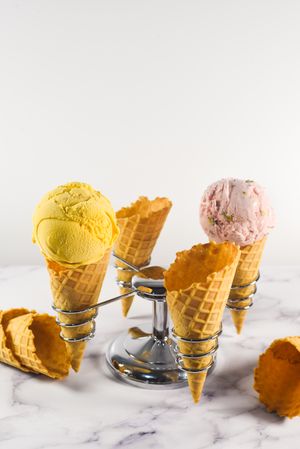 Ice cream cone stand with waffle cones and pink and purple scoops, vertical