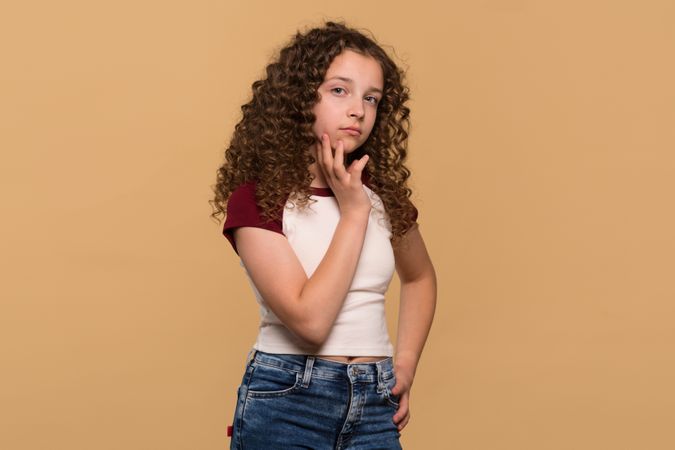 Thoughtful young girl resting chin on hand, looking serious
