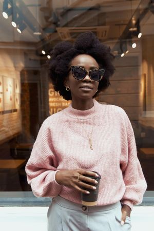 Woman in pink sweater wearing sunglasses standing beside store front