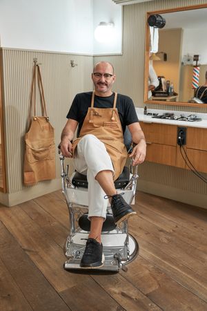 Confident smiling barber sitting on chair in barbershop