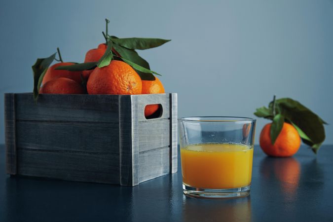 Box of tangerines, and glass of juice on blue background