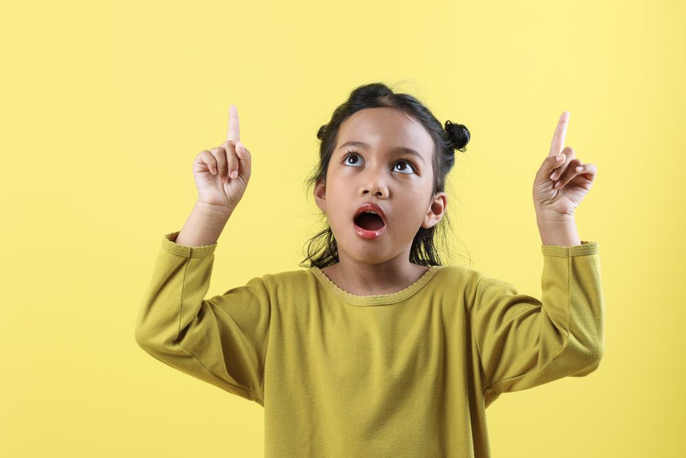 Positive Asian Little Girl Points Above Show Place for Advertising Text Surprised