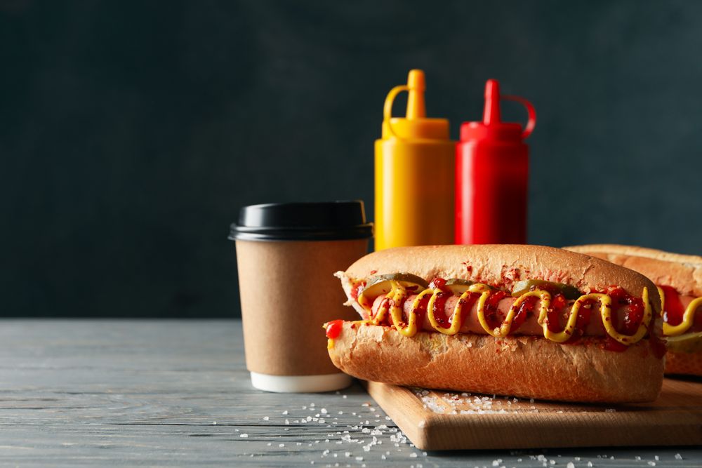 Tasty hot dogs, coffee and sauces on wooden background