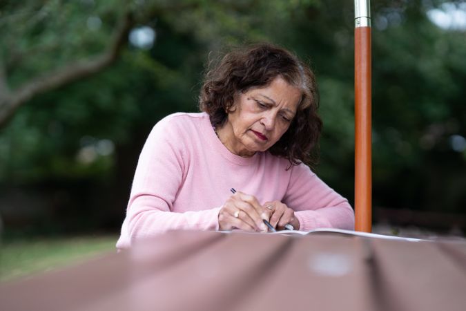 Older woman drawing on park bench among greenery