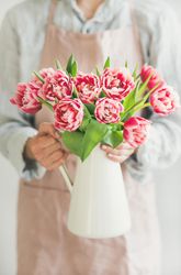 Florist wearing pink apron holding vase with bright spring flowers
