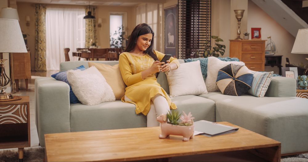 Young Indian Woman Exploring Internet Trends, Using Smartphone On Sofa, Does Online Shopping, Remote Work from Home.