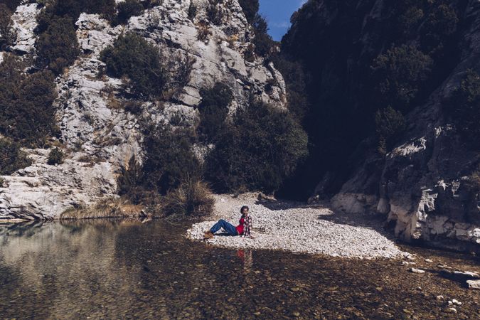 Positive woman resting on stone shore near river