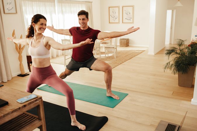 Couple exercising yoga indoors following instructions on laptop