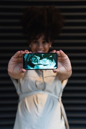 Smiling Black woman showing smartphone screen with baby ultrasound