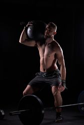 Strong sportsman with weight ball on shoulder performing exercis
