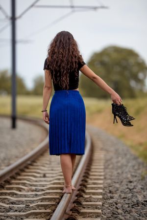 Woman walking on the train railings barefoot holding her heels