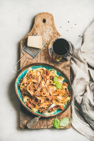 Pasta dinner with minced meat, cheese and red wine on wooden board atop marble counter