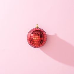Red Christmas disco ball bauble on pink background with shadow