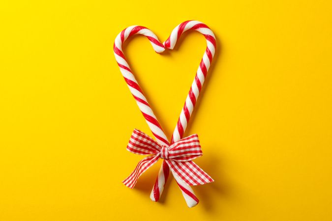 Sweet candy canes with bow on yellow background, space for text