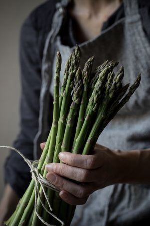 Faceless woman holding bundle of green asparagus