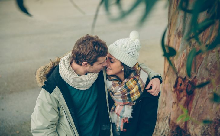 Couple about to kiss in winter coats embracing under tree