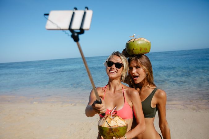 Female friends taking picture with smartphone on selfie stick on beach