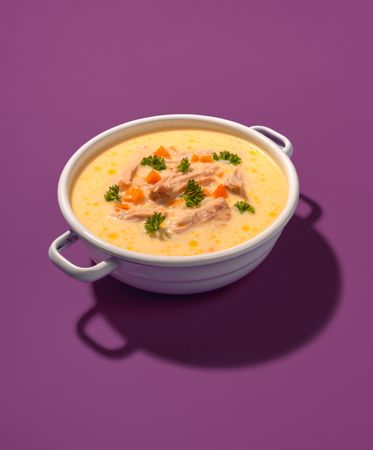 Chicken soup bowl, greek recipe, isolated on a purple background