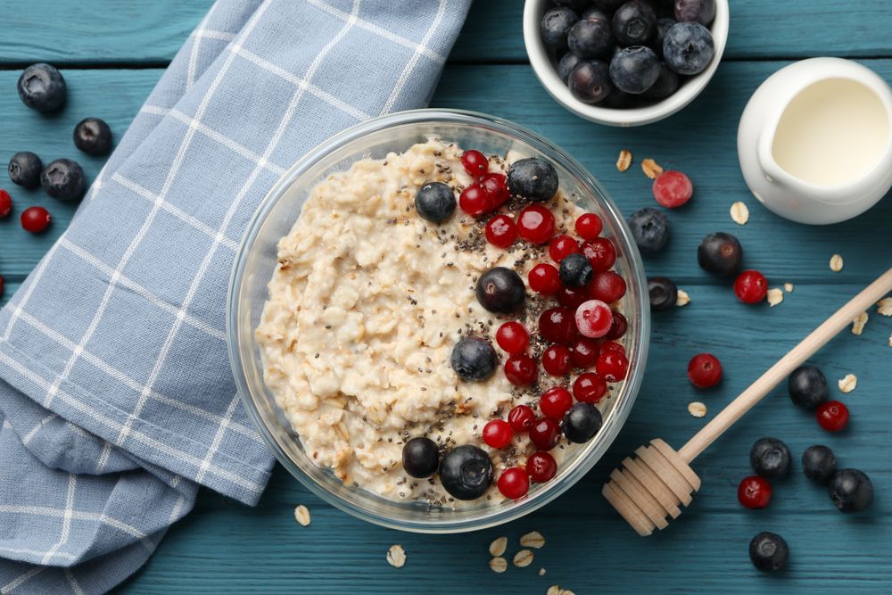 Towel and bowl with oatmeal porridge and fruits on wooden background. Cooking breakfast