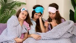 Three girls feeling sick, checking temperature at home.