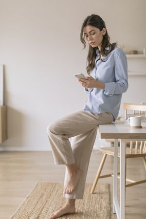 Woman leaning on dining room table holding a smart phone