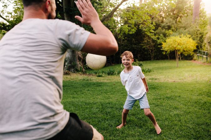 Happy little boy playing passing the ball game with his father