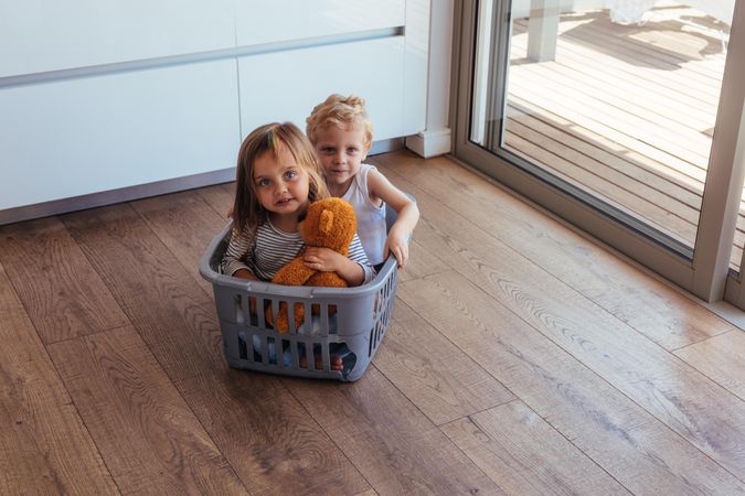 Beautiful young children sitting in a washing basket at home
