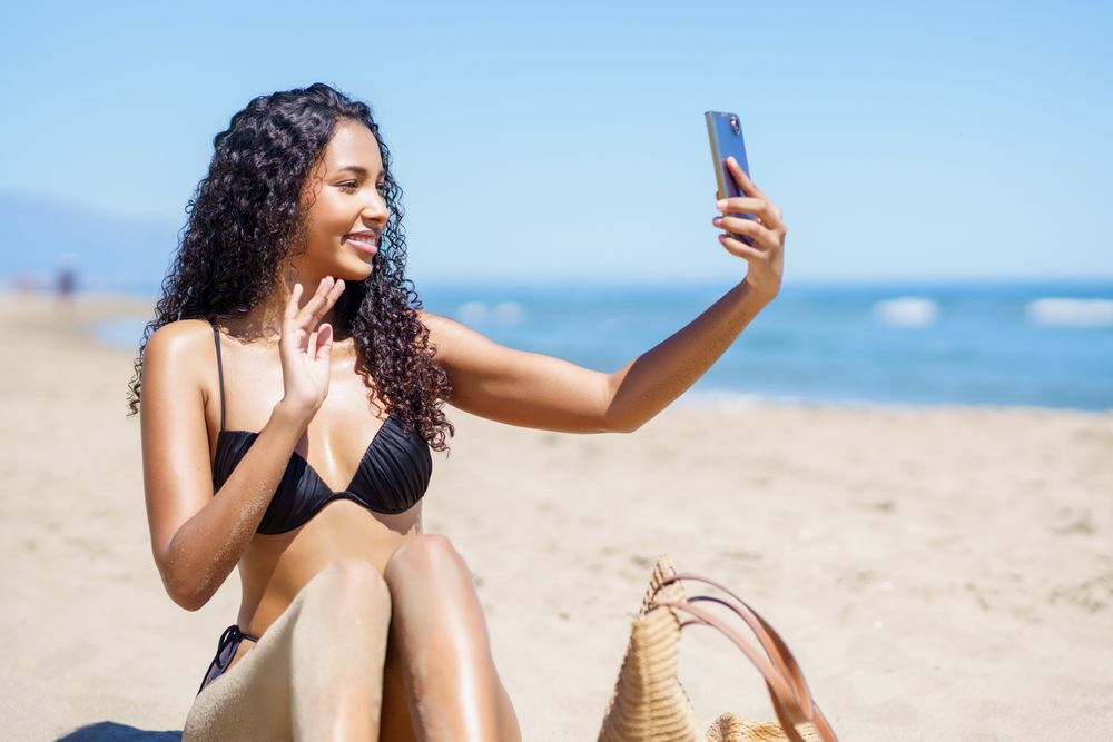 A Young Woman Happily Enjoying a Beautiful Sunny Day While Taking a Fun Selfie at the Beach