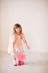 Girl in pink dress holding a balloon against light background