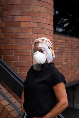 Portrait of Black female nurse in face shield, N95 mask, scrubs and hair wrap
