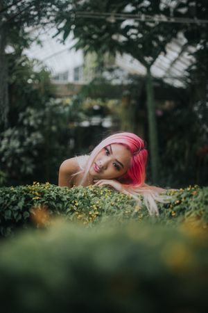 Woman with pink hair leaning her head on bush