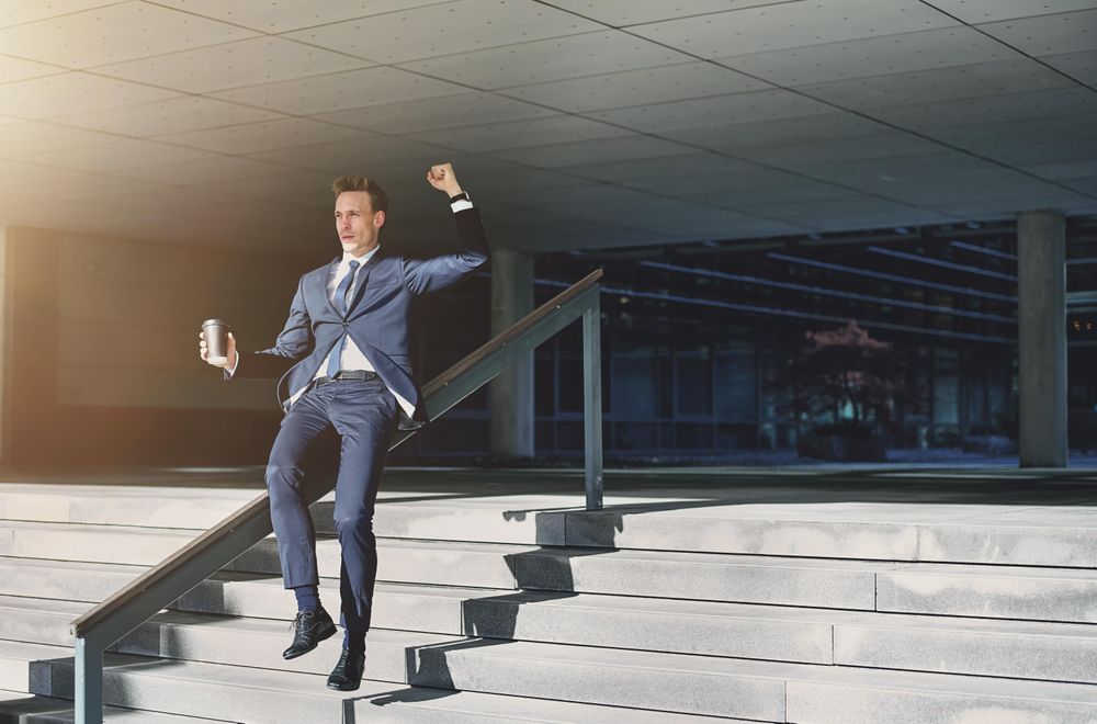 Man in business attire slides down a handrail outside