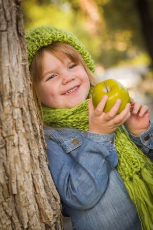 Young Girl Wearing Green Scarf and Hat Eating Apple Outside