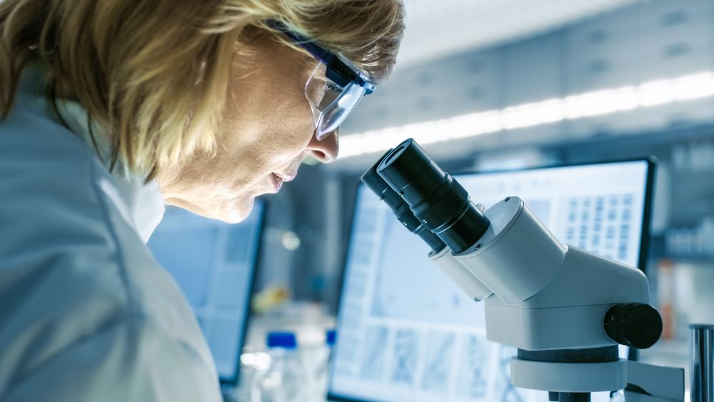 Mature Female Biologist Works on Her Computer and Looks at Materials under Microscope.
