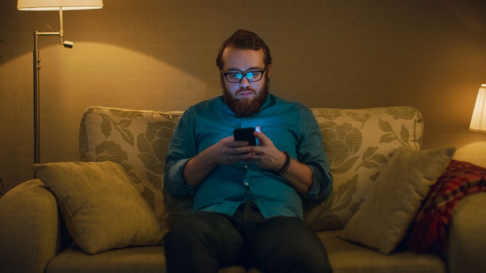 Portrait Shot of a Man Sitting on a Sofa in His Living Room, Using Smartphone.