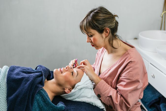 Beautician plucking eyebrows on face of woman in salon