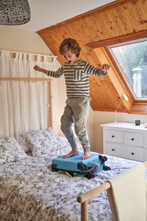 Cheerful boy jumping on suitcase