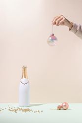 Woman’s hand holding Christmas tree decoration with champagne bottle
