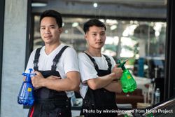 Two men in overalls standing in auto detail shop holding water bottles benWK0